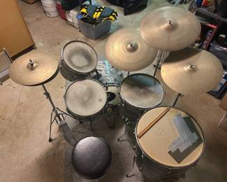 This drum set includes a bass drum, two mounted toms, a floor tom, and a snare in a marbled silver-gray wrap, paired with four cymbals on stands including a hi-hat with pedal. A bass drum pedal, hardware stands, drum sticks, and a round padded throne are included. Shells and heads show playing wear including tape on the bass drum head — a solid practice or project kit.
