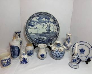 This lot brings together blue-and-white Delft-style pieces including a large windmill scene charger plate, a bulbous tulip vase with multiple spouts, two bottle-form vases, a small windmill figure, a candlestick, a decorative wall plate on a stand, a small mug, and several assorted vases and jars. All share the traditional cobalt-on-white palette with Dutch landscape and floral motifs. A cohesive grouping for a collector or a blue-and-white display shelf.
