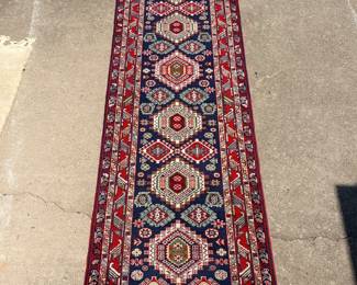 This long runner rug features a row of stepped hexagonal medallions in red, green, and ivory against a deep navy field, framed by multiple patterned borders in red and ivory. Both ends finish in natural fringe, and the pile appears clean and even throughout. A handsome runner for a hallway, entry, or long narrow space.
