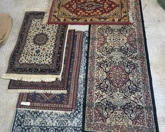 This lot includes six smaller rugs and mats in traditional patterns: a red and ivory medallion mat, an ivory-field floral piece with navy border, a long black-bordered runner with a red and ivory medallion design, a navy geometric piece, a light blue and ivory floral mat, and one additional rolled rug. Sizes range from doormat scale up to runner length. A practical multi-room lot or a good buy for resellers.