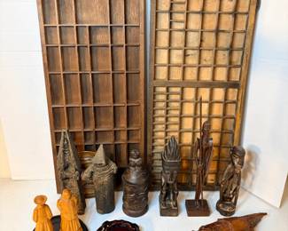 This lot pairs two wooden printer's type trays with divided compartments — popular for shadow-box display of small collectibles — with a group of carved wood and composition figures including robed and standing figures, a small pitcher, and a carved leaf-form piece of wood. Materials and origins vary across the figures. A good starting lot for a curio display or shadow box project.