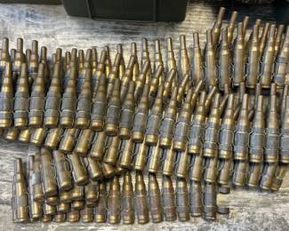This lot consists of a large spread of brass-linked belt ammunition, likely .30 caliber or similar, in the distinctive linked-carrier configuration used in belt-fed machine guns. Linked military ammunition belts like these are popular with militaria collectors, WWII and Cold War reenactors, and shooters who reload or collect inert display pieces. A visually striking lot with strong militaria shelf appeal.