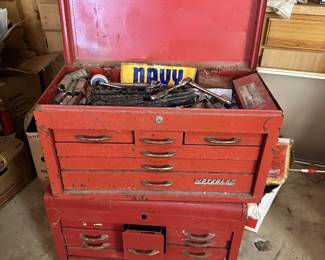 Red metal machinist tool chest with small drawers and hand tools.