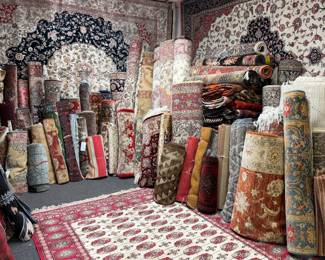 Warehouse view showcasing a large assortment of rolled and displayed rugs in traditional patterns.