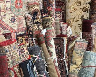 Rolled rugs featuring warm gold, red, blue, and neutral tones.