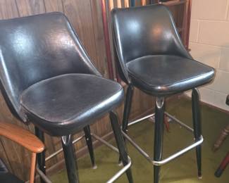 vintage black vinyl swivel bar stools with bucket-style seats, a metal frame, and a circular footrest ring, resembling mid-century modern designs such as the Dutchess Line or similar 1960s/1970s commercial bucket bar stools