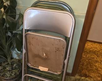 stack of vintage metal folding chairs with olive-green or gray-green frames and brown padded vinyl backrests and seats