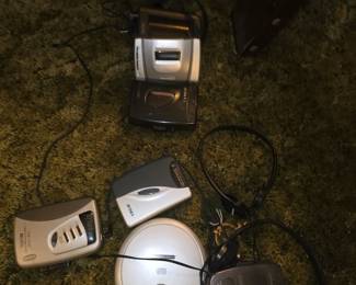 The image shows a collection of vintage portable audio devices, including cassette players, a portable CD player (Discman), and wired headphones