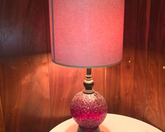 ruby red or cranberry embossed glass globe table lamp with a dark metal base and a cylindrical pinkish-purple fabric shade.