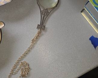 This is a vintage Florenza magnifying glass pendant necklace featuring an ornate, Victorian-revival silver- or gold-toned filigree frame shaped like a stylized antique key with a matching long chain.