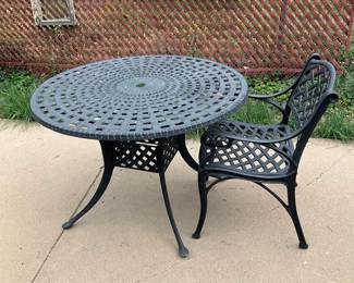 Cast Aluminum Outdoor Patio Set — Sturdy cast aluminum patio table and matching armchair with classic lattice design and powder-coated finish. The round table features an umbrella hole and curved tripod legs while the chair includes a contoured seat and decorative scrollwork on the arms and back. Table measures approximately 29 in high with a 42 in diameter top; chair is approx 34 in high, 23 in wide, seat depth 18 in. Overall good condition with surface wear and some faded paint from outdoor exposure; no visible structural damage but may benefit from repainting or touch-up.