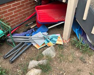 Assorted Outdoor Gear Lot — A mixed lot of outdoor and yard items including a red plastic sled, folded beach or camping chairs with metal frames, and a striped fabric beach umbrella or canopy cover. The items show outdoor wear and dirt consistent with storage on the ground; plastics and metal frames appear intact but need cleaning and possible minor rust treatment. Overall dimensions represent the largest item (sled) at roughly 40 inches long and pile measures about 40 x 24 x 8 inches; lightweight components are easy to carry but bulky. Priced for quick estate-sale pickup in Breckenridge, items are sold as-is with no guarantee of structural integrity or completeness.