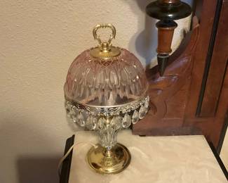 Cut Crystal Teardrop Table Lamp — Decorative cut-glass table lamp with a pink-tinted pressed-glass dome shade, brass-plated base and ornate brass finial. The shade features molded teardrop patterning and a decorative brass band with hanging crystal prisms; the clear glass stem echoes the domed motif. Functional electric lamp with cord shown; good overall cosmetic condition with light surface wear and minor age patina to the brass. Measures compactly and works well as a bedside or accent lamp.