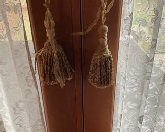 Pair Ornamental Curtain Tassels — Pair of decorative curtain tassels with turned wooden finials and twisted cord hangers, shown hanging from brass door levers. Neutral beige/gold fibers with braided necks and full looped skirts; one tassel's ribbon hanger is frayed. Good overall decorative condition with light wear consistent with use; sold as a matching pair. Useful for draperies, French doors, or as decorative hardware accents.