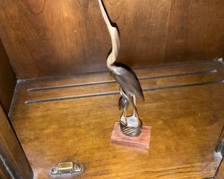 Brass Heron Bird Sculpture on Wood — Decorative brass heron sculpture mounted on a small wooden base with an elegant elongated neck and stylized form. The piece appears to be cast brass with a warm patina and sits on a rectangular rosewood-toned base, suitable for a shelf or mantel. Overall height is modest and it's light enough for easy placement in a living room or office display. Condition is good with surface patina and minor surface wear consistent with age; base shows small scuffs but no structural damage.