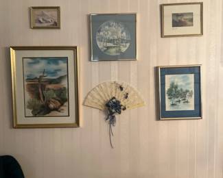 Wall Gallery of Framed Prints & Fan — Eclectic wall gallery featuring five framed artworks and a decorative folding fan mounted in the center. The collection includes several small watercolors/prints in gold and silver frames with matting and a cream lace decorative fan embellished with ribbon and fabric flowers. Overall display measures approximately 42 inches wide and 40 inches tall; each smaller frame ranges from about 6–14 inches in width, and the fan is roughly 14 inches wide. Items are in good condition with light age-related wear to frames and paper and appear ready to hang as-is or be reconfigured to suit a buyer's space.