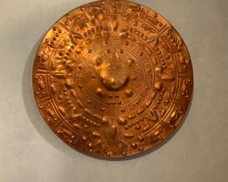 Embossed Copper Wall Plaque — Decorative embossed copper wall plaque with a raised central boss and concentric ornamental bands showing stylized faces, dots and floral motifs. The piece is hand-hammered or repoussé-style metal with a warm polished copper patina and appears to be a lightweight decorative disk suitable for wall display. No maker's marks or dates are visible in the photos; condition is good with light surface scratches and minor toning consistent with age and handling. Measures approximately 18 inches across and is thin enough to hang with basic hardware.