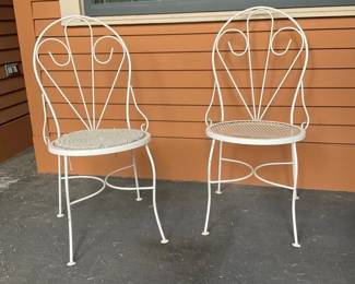 White Wrought Iron Patio Chairs (pair) — Pair of white wrought-iron patio chairs with decorative fan-back design and mesh seats, ideal for a small porch or bistro set. Constructed from tubular metal with curved legs and scrolled back details; one seat shows a thin round cushion while the other is bare. Each chair is a lightweight, stackable-style outdoor chair — estimated dimensions provided for transport and staging. Overall good condition with surface paint wear, minor rust spots, and typical outdoor weathering; structurally sound and ready for use or repainting.