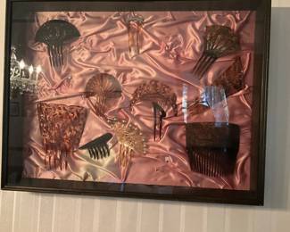 Framed Vintage Hair Comb Display — Framed shadowbox featuring a collection of vintage hair combs and decorative hairpins mounted on pink satin backing. The wooden frame holds a variety of celluloid, tortoiseshell-style, and metal decorative combs in different sizes and styles, making a decorative wall statement for a bedroom or dressing room. Overall frame measures approximately 24 in wide, 18 in tall and 1.5 in deep; lightweight and easy to hang. Good estate-sale condition with intact glass and minor surface wear to the frame and backing; combs appear complete though not tested for fragility or restorations.
