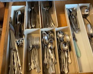 Mixed Stainless Flatware & Utensils Lot — Large kitchen drawer lot of mixed stainless flatware and cooking utensils including forks, knives, spoons in cardboard dividers plus ladles, spatulas, tongs, whisks, peelers, thermometers, long-reach lighters and other common kitchen tools. Pieces are a mix of stainless steel and plastic-handled tools showing normal kitchen wear with some minor surface scratches and light tarnish on silverplate pieces; overall serviceable for everyday use. Good assortment for stocking a household or for use as backup/party flatware; utensils are loose and not a branded matched set. Overall condition is good given age and use; see photos for exact patterns and wear.