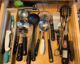 Mixed Stainless Flatware & Utensils Lot — Large kitchen drawer lot of mixed stainless flatware and cooking utensils including forks, knives, spoons in cardboard dividers plus ladles, spatulas, tongs, whisks, peelers, thermometers, long-reach lighters and other common kitchen tools. Pieces are a mix of stainless steel and plastic-handled tools showing normal kitchen wear with some minor surface scratches and light tarnish on silverplate pieces; overall serviceable for everyday use. Good assortment for stocking a household or for use as backup/party flatware; utensils are loose and not a branded matched set. Overall condition is good given age and use; see photos for exact patterns and wear.