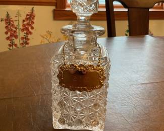 Cut Glass Decanter with Brass Label — Attractive pressed-cut glass decanter featuring a faceted stopper and decorative brass label on a chain. The square-bodied decanter has an allover starburst pattern in clear glass and a heavy feel typical of mid-century barware. Overall height approximately 9.5 in with a 3.5 in width and 3.5 in depth, a solid piece suitable for display on a home bar or dining room sideboard. Good condition with no visible chips or cracks; brass label shows light surface wear and patina consistent with age.