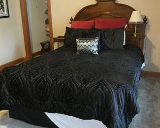 Ornate Carved Wood Full Bed Headboard — Solid carved wood headboard with ornate finials and curved crest rail shown mounted to a full/queen bed setup; warm medium-brown finish and classic turned finial accents give it traditional character. Construction appears sturdy with visible wear consistent with normal use — small surface scratches and minor finish loss in places but no major structural damage visible. Works well as a focal point for a traditional bedroom or to pair with restored vintage case pieces; headboard is shown with bedding for scale. Overall condition is good and ready to reuse or refinish to taste.
