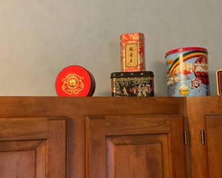 Decorative Metal Tea Tin — A decorative round metal tea tin with colorful printed graphics and a removable lid; pictured among several assorted collectible tins. The tin appears to be mid-size, painted with bright scenes and gold-tone trim visible on some pieces; ideal for storage or display in a kitchen or pantry. Condition is good for display with light surface wear and minor scuffs consistent with shelf use; lid appears to fit. Measurements are approximate.
