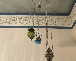 Three Hanging Glass Pendant Ornaments — Set of three decorative hanging pendant ornaments with colored glass bodies and ornate metal caps and finials. Each pendant hangs from a beaded chain: one green glass ornament, one turquoise/blue glass ornament, and one mauve/pink glass ornament with decorative silver-toned metalwork. Overall hanging length from ceiling plate to bottom finial measures approximately 30 in; pendants themselves range about 4 in tall and 3 in wide, making them suitable for accent lighting or decorative display. Items show light surface wear consistent with normal use but appear structurally intact with no obvious cracks in the glass.