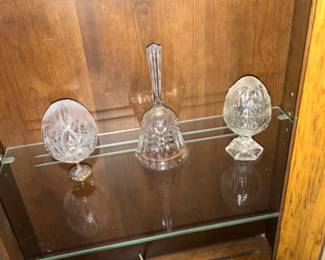 Cut Crystal Bell & Egg Ornaments Set — A small grouping of cut crystal decorative pieces including a tall-handled crystal bell flanked by two egg-shaped crystal ornaments on pedestal bases. Each piece features classic faceted/cut patterns that catch light and are ideal for a curio cabinet or holiday display. Overall compact display pieces — bell approx. 6.5 in tall, eggs approx. 3.5–4 in tall each — lightweight and easy to move. Good estate condition with light shelf wear and no obvious chips or cracks visible in photos.