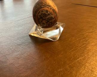 Polished Decorative Stone Egg on Crystal — Attractive polished stone egg presented on a faceted clear crystal or acrylic display stand, perfect as a small accent for a mantel or desk. The egg shows natural banding and spotted patterning in warm brown, tan and gray tones and appears hand-polished to a soft sheen. Overall compact size makes it easy to place — stand plus egg are lightweight and simple to display. In good condition with no visible chips or cracks to the stone or stand; recommended as decorative or for a collector of polished minerals.
