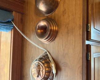 Copper Hanging Molds Set — A trio of vintage copper hanging molds in mixed shapes including a shallow heart/oval, a fluted ring mold, and a decorative fruit-motif mold. Each piece shows the warm patina and light surface wear consistent with age; no visible major dents but there is general tarnishing and small surface scratches. These wall-mounted molds make attractive kitchen decor or collectible display pieces and are lightweight enough to rehung individually. Overall condition is good for decorative use; measurements below are approximate.