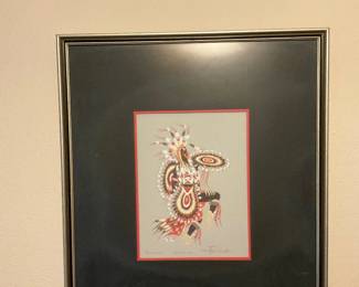 Framed Native Dancer Print — Framed print depicting a Native dancer in full regalia with red matting and wide black double mat. The piece is under glass in a slim silver-tone frame and appears to be a signed limited print (signature visible lower right) — good decorative quality for a hallway or entry. Frame shows light surface wear and the mat has minor handling marks; glass intact. Overall size is moderate and ready to hang as shown.