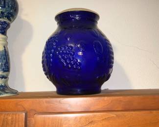 Cobalt Blue Embossed Glass Vase — Large cobalt blue blown glass vase with pronounced embossed grape-and-oval motif and a wide rolled rim. The piece has a heavy, thick-walled feel typical of decorative art glass and displays deep, even cobalt color that remains vivid in photos. No maker marks are visible; condition appears good with light surface wear and no obvious chips or cracks in the photographed areas. Stands substantial enough for display or as a floor vase for dried stems.