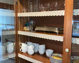 Oak China Cabinet with Glass Doors — Solid oak china cabinet with glass-paneled doors and adjustable shelving shown with lace shelf trim. The cabinet features brass hardware, plated shelf standards for adjustable heights and a warm medium oak finish; doors close with visible round ceramic knobs. Good solid condition with light surface wear and small scuffs consistent with normal use; glass panels intact. Overall practical storage for dinnerware or display, measures approximately as shown below.