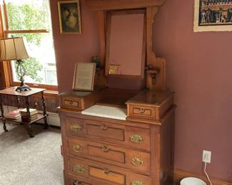 Oak Dresser with Mirror and Marble — Solid oak dresser with an attached carved mirror frame and inset white marble top over the center drawer. The piece shows classic late-19th/early-20th-century styling with carved apron, original brass hardware, and small side pedestals flanking the mirror. Good structural condition with expected surface wear, light finish loss, and small scratches consistent with age; mirror glass intact. Overall a sturdy, attractive bedroom dresser that would clean and refinish nicely or remain as a character piece.