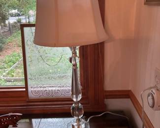 Crystal Table Lamp with Fabric Shade — Elegant crystal table lamp with a tapered fabric shade offering classic bedside or entryway lighting. The lamp features a faceted crystal base and stem with polished metal accents and a white/ivory bell-shaped shade. Overall height is appropriate for side table use and the clear crystal reflects light attractively; perfect for traditional or transitional interiors. In good used condition with light surface wear on metal fittings and the shade showing minor discoloration near the top edge.