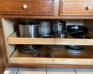 Mixed Kitchenware Lot — A large lot of everyday kitchenware including nested stainless mixing bowls, metal cake pans and molds, colanders, a few nonstick frying pans, glass lids, assorted baking tins, plastic storage lids, and small appliances/attachments (hand blender parts and food-processor bowl/blade shown). Pieces are mixed metals, glass and plastic with visible wear and light staining on some cookware; overall serviceable for home use or as backup pieces. No major brand markings visible in photos; items sold as-is and sold together as one lot. Estimated combined size and weight below reflect the full grouped contents.