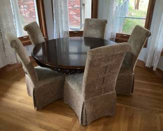 Carved Pedestal Round Dining Table — Solid wood round dining table with a carved central pedestal and scrolled tripod base, shown with six slipcovered high-back chairs. The rich dark finish and carved apron/leg details give it a traditional, formal look; pedestal construction allows generous legroom. Tabletop shows light surface wear and some small finish scuffs consistent with normal use; base carving and chair slipcovers are intact though chairs show light fabric wear. Measures roughly 48 inches diameter and standard dining height; sturdy, heavy construction will require two people to move.