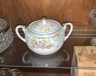 Floral Porcelain Covered Sugar Bowl — Charming porcelain covered sugar bowl decorated with hand-painted pastel floral sprays and gilt trim. The two-handled design and matching lid feature soft blue banding and small pink and yellow flowers over a white ground. Measures approximately 4.5 inches tall (with lid) and 7.5 inches wide from handle to handle, a compact piece suitable for dining-room service or decorative display. Good estate condition with light surface wear and minor gilt loss consistent with use; no visible chips or cracks.