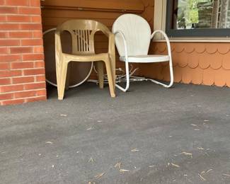 Plastic Patio Chairs (Pair) — Pair of outdoor patio chairs consisting of one molded tan plastic stacking chair and one white metal-framed lawn/glider-style chair with molded seat. Both are suitable for porch or patio use; the plastic chair is lightweight and stackable while the white chair has tubular metal arms and a spring base. Overall dimensions per chair are small and easy to move — see measurements below for estimates. Both chairs show outdoor wear and surface dirt with some rust spots on the metal frame and sun-fading on the plastic; sold as-is and priced to move for estate sale pickup.