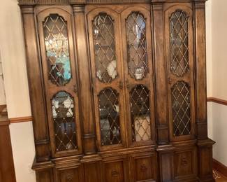 Large Carved Wood China Cabinet — Impressive large carved wood china cabinet with four glass-front doors and diamond-pattern mullions, offering elegant display and lower storage. Constructed from heavy stained hardwood with molded cornice, fluted pilasters, brass hardware and multiple lower cupboard doors for concealed storage. Overall footprint is substantial — ideal for dining room display of china, crystal and collectibles; measurements provided for moving and placement. Good estate condition with light surface wear and minor finish scuffs consistent with age; glass intact and hardware functional.