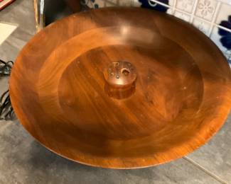 Large Turned Wood Serving Bowl — Solid turned wood serving or display bowl with warm grain and a center knob typical of mid-century handcrafted bowls. The bowl shows attractive natural wood patterns and a smooth finish with light surface wear and small dings consistent with normal use. Sturdy, decorative piece that works well as a centerpiece or for holding fruit and linens; no maker's marks visible. Approximately 16–18 inches across and shallow in profile, it is a substantial single-piece bowl in good usable condition.