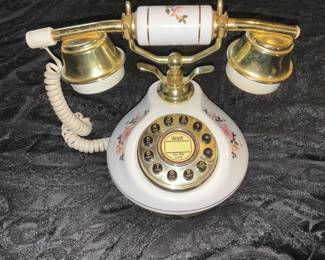 Porcelain Floral Retro Rotary Phone — Decorative porcelain rotary-style telephone with floral transfers and gold-tone hardware. The handset and base are white porcelain with pink/orange floral motifs and gold-painted metal accents; rotary dial is labeled with a center "wait for dial tone" decal. Unit shows light surface wear and minor gold loss on handset cups and base hardware but no visible cracks in porcelain; cord is coiled and intact though may be nonfunctional for modern lines. Compact decorative piece that measures small enough for a bedside table or desk.
