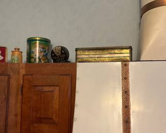 Decorative Metal Tea Tin — A decorative round metal tea tin with colorful printed graphics and a removable lid; pictured among several assorted collectible tins. The tin appears to be mid-size, painted with bright scenes and gold-tone trim visible on some pieces; ideal for storage or display in a kitchen or pantry. Condition is good for display with light surface wear and minor scuffs consistent with shelf use; lid appears to fit. Measurements are approximate.