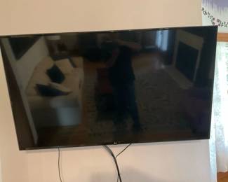 LG 55" LED Flat Screen TV — LG 55-inch LED flat screen TV shown wall-mounted with visible LG badge on the lower bezel. Good mid-size television for bedroom or living room use; slim bezel and flat-panel design keep a clean profile. Appears to be in working order (screen is intact with no visible cracks) though only powered-off photos are provided; cords visible but no remote or original box shown. Cosmetic condition is good with light surface marks and typical handling wear around the mount area. Overall dimensions listed below approximate the screen footprint.