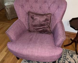 Button-Back Pink Accent Chair — Upholstered button-back accent chair in a muted pink/lavender fabric with nailhead trim along the arms and tapered dark wood legs. The wing-style back with tufted buttons and included plush throw pillow make it a comfortable occasional chair for a living room or bedroom. Shows light, even wear consistent with normal use; fabric appears intact with no visible rips or stains in photos. Compact footprint works well in smaller rooms — see dimensions for sizing.