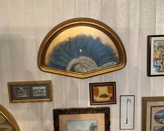 Framed Decorative Blue Hand Fan — Decorative hand fan displayed in a custom gold half-moon frame, featuring blue silk or feathered upper sections with a lace and painted paper lower fan leaf. The fan is mounted behind glass in a shallow domed frame suitable for wall display and pairs well with traditional or Victorian-style decor. Overall wall piece appears medium-sized (see dimensions) and lightweight for easy hanging; ideal as an accent in living rooms, hallways or entryways. In good estate condition with minor age-appropriate discoloration to paper and slight wear to fabric/feathers but frame and glass intact.