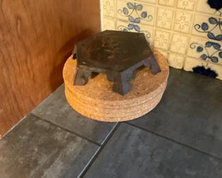 Small Hex Cast Iron Trivet — Heavy small hex-shaped cast iron trivet with six short bracket feet and a flat top surface. Solid, utilitarian piece likely used for hot pots or as a small stand; the iron shows surface rust and patina consistent with age and use. Sturdy construction and compact footprint make it useful as a decorative kitchen stand or plant riser; measures small enough for tabletop use. Condition is fair with visible rust and wear but structurally sound.