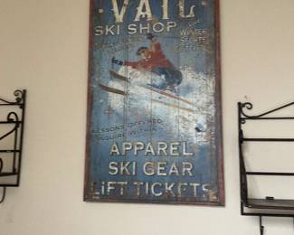 Vail Ski Shop Wood Sign — Large rustic wooden advertising sign reading "VAIL SKI SHOP" with painted skier artwork and distressed blue background. The piece has a vintage lodge style, framed with a narrow red border and shows surface wear, paint loss and scuffs consistent with age and use. Good decorative condition for chalet or ski-themed rooms; lightweight wood construction makes it easy to hang. Overall measurements provided are approximate.